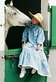 Mädchen auf einer Stalltür sitzend beim Küssen ihres Pferdes