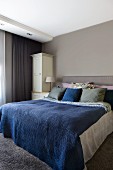 Doppelbett mit blauer Tagesdecke in hellgrau getöntem Schlafzimmer