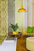 House plant on wooden table, yellow chair and pouffe in front of lengths of wallpaper