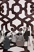 Various monochrome paints in glass jars on length of black and white patterned wallpaper