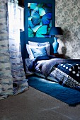 Bed with blankets, pillows and scatter cushions in shades of blue below picture of bright turquoise and blue butterflies