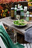 Bottles of wine in wire baskets, dish of salad and bottles of dressing on rustic table; autumnal vine foliage in background