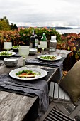 Herbstliche Stimmung über rustikal gedecktem Tisch mit Pizza und Salat; Blick auf norwegische Schärenküste im Hintergrund