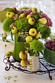 Flower arrangement with green carnations, sedum and crab apples in various vases on small wire tray