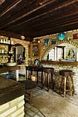 Küche in brasilianischem Kulthaus mit Klinkerwänden und dunkler Holzdecke; rustikale Barhocker vor gemauertem Rundbogen und Darstellungen der Meeresgöttin des Candomble
