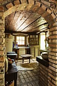View through brick archway into rustic kitchen with dark wooden ceiling, brick floor and walls
