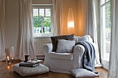 Comfortable armchair, floor cushions and elliptical lamp in corner of living room