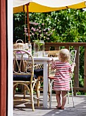 Kleinkind in Sommerkleidchen steht am Terrassentisch