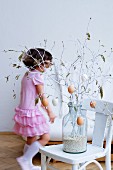 Little girl in pink dress behind Easter bouquet of white-painted spring branches