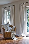 Comfortable wicker chair in front of windows with over-long curtains