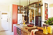 Modern, country-house kitchen with kitchen utensils hanging from rack above island block