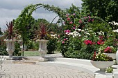 Lavish garden with climbing roses; planted stone urns and bowls in foreground