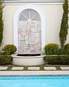 Arched window filled with mosaic of stone tiles and small fountain