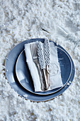 Hand-crocheted knife covers on knives and blue plate on white artificial snow
