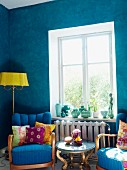 Living room with bright blue walls, antique upholstered armchairs, small side table & standard lamp