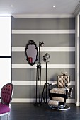 Gepolsterter Vintage Friseurstuhl neben Scheinwerfer Stehleuchte vor grau weiss gestreifter Wand, im Vordergrund Neo Rokoko Stuhl