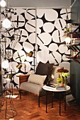 Wire-framed standard lamp in seating area in front of black and white patterned wall