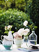 Gestapelte Vintage Tassen und weiße Rosen in Flaschen auf Tisch im Freien