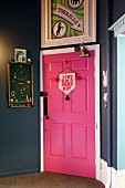 Pink door in hallway painted dark grey with framed poster and pinboard