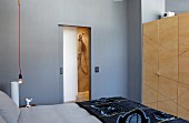 Graues Schlafzimmer mit hellen Holzfronten und Doppelbett mit harmonierender Bettwäsche; das Badezimmer ist durch eine Schiebetür direkt verbunden