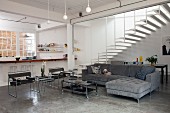 Modern, open-plan interior with polished concrete floor, Wassily chairs and large chaise sofa; wide, airy staircase in background