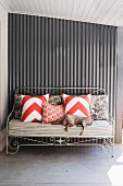 Dog on upholstered metal bench with scatter cushions against metal wall of veranda