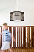 Child on gallery with balustrade of wooden rods and designer pendant lamp