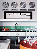 Modern kitchen with green mosaic wall tiles; four clocks showing different times on wall above shelf