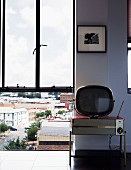 Floor-to-ceiling window with view of cityscape; retro radio and retro TV against wall