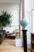 Globe on black plinth in front of seating area with leather sofa and armchair next to designer lamp made of rings in traditional interior