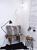 Grey and black scatter cushion on Africa wooden stool and black, animal-skin rug in corner of white room