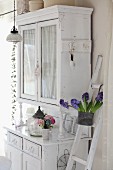 White, distressed dresser with shabby chic ornaments and blue hyacinths in pot hanging from ladder
