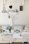 Retro, industrial-style pendant lamp above breakfast table daintily set with white china and blue grape hyacinths; shabby chic ornaments on wall hooks in background