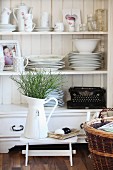 Floral crockery, photo of child and old typewriter on open shelves behind bouquet in enamel jug and Easter eggs