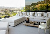 White sofa combination in corner of living room with panoramic view over city and landscape reflected in glass wall