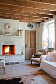 Pale upholstered furnishings, shabby-chic decor on mantelpiece above blazing open fire in cosy interior