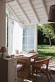 Sunny breakfast area with wicker chairs and rustic wooden table in white-painted conservatory extension