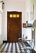 Various metal chairs against wall on chequered floor in foyer and old wooden door with square glass panels