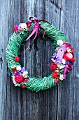 Willow wreath with multicoloured flowers and fruits on wooden wall