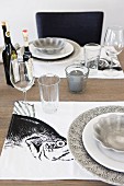 Tischgedecke mit grauen Tellern auf schwarzweissen Sets mit Fischmotiv