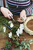 Florist's hands arranging yarrow and sprigs of berries on straw wreath on garden table