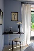 Narrow table with lamp and decoration in front of dove-grey wall in bedroom