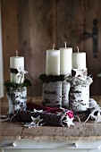 weiße, weihnachtlich dekorierte Stumpenkerzen auf Birkenästen als Kerzenständer und farbige Strickgarnrollen auf Holzunterlage