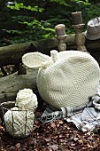 White, crocheted, apple-shaped cushion and ball of wool in wire basket on woodland floor