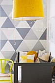 Pale grey cot against wall with painted grey geometric pattern and yellow pendant lamp in foreground