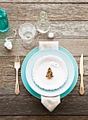 Pale blue place setting with silver cutlery and Christmas-tree biscuit on rustic, weathered wooden table