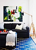Coffee table, black sofa, patterned rug, modern artwork, standard lamps with wooden frame and black lampshade in living area