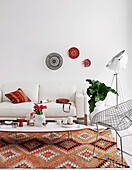 White upholstered sofa and wire mesh chair around classic coffee table on folkloric carpet