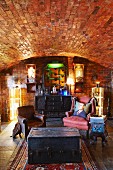 Dark wooden trunk in front of old leather armchairs in cellar-type room with brick barrel-vaulted ceiling
