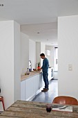 View through floor-to-ceiling doorway of man at kitchen counter in minimalist interior